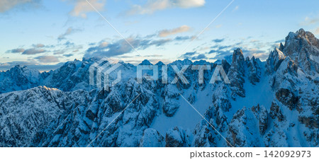 Panoramic winter view of the Dolomites at sunset with dramatic rocky peaks and snow covered ridges under colorful clouds, showcasing majestic alpine scenery in high resolution. Panoramic winter view of the Dolomites at sunset with dramatic rocky peaks and snow covered ridges under colorful clouds, showcasing majestic alpine scenery in high resolution. 142092973