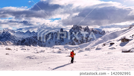 Ski mountaineer crossing a snowy ridge in the Dolomites with dramatic alpine peaks and blue sky in the background, capturing winter adventure and breathtaking mountain landscape. 142092991