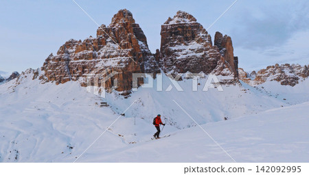 Ski mountaineer crossing a snowy ridge in the Dolomites with dramatic alpine peaks and blue sky in the background, capturing winter adventure and breathtaking mountain landscape. 142092995