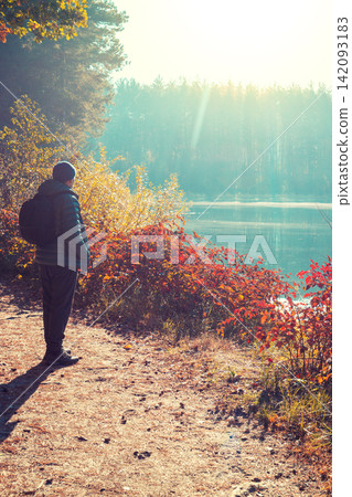 Man tourist stands on a picturesque lakeshore in the autumn morning and looking at the sunrise Man tourist stands on a picturesque lakeshore in the autumn morning and looking at the sunrise 142093183