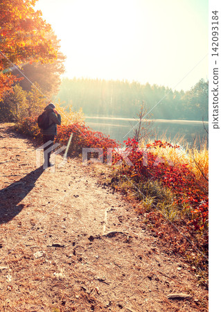 Man tourist stands on a picturesque lakeshore in the autumn morning and looking at the sunrise Man tourist stands on a picturesque lakeshore in the autumn morning and looking at the sunrise 142093184