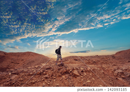 Human hiking in a desert. Desert landscape with dramatic cloudy sky Human hiking in a desert. Desert landscape with dramatic cloudy sky 142093185