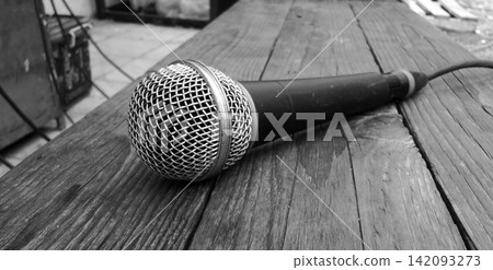 Black and white wired microphones on a rustic wooden table. Black and white wired microphones on a rustic wooden table. 142093273