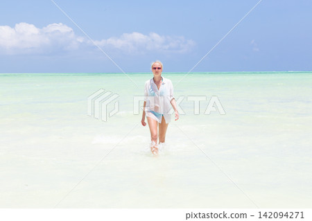 Happy woman having fun, enjoying summer, walking along white tropical beach. Beautiful caucasian model wearing white beach tunic on vacations on picture perfect Paje beach, Zanzibar, Tanzania. Happy woman having fun, enjoying summer, walking along white tropical beach. Beautiful caucasian model wearing white beach tunic on vacations on picture perfect Paje beach, Zanzibar, Tanzania. 142094271