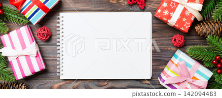 Top view of a notebook on wooden holiday background made of fir tree and New Year decorations. Christmas time concept Top view of a notebook on wooden holiday background made of fir tree and New Year decorations. Christmas time concept 142094483