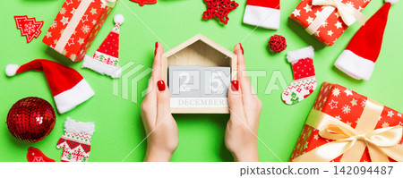 Top view of female hands holding calendar on green background. The twenty fifth of December. Holiday decorations. Christmas time concept Top view of female hands holding calendar on green background. The twenty fifth of December. Holiday decorations. Christmas time concept 142094487
