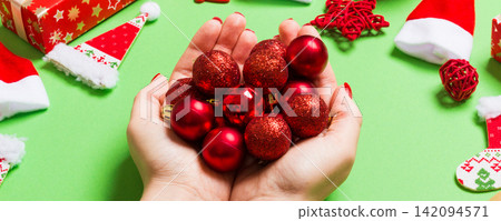 Top view of a heap of New Year balls in female hands on green backround made of festive decorations. Christmas time concept 142094571