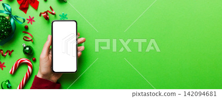 christmas mockup with space for text. christmas advertising, app template. hand holding phone with empty screen on table background. Happy New Year and Xmas Flat lay 142094681