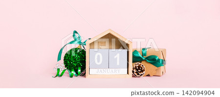 1 january. Christmas composition on colored background with a wooden calendar, with a gift box, toys, bauble copy space 1 january. Christmas composition on colored background with a wooden calendar, with a gift box, toys, bauble copy space 142094904