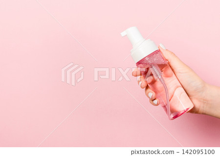 Female hand holding spray cream bottle of lotion isolated. Girl give cosmetic products on pink background Female hand holding spray cream bottle of lotion isolated. Girl give cosmetic products on pink background 142095100