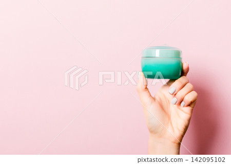 Female hand holding cream bottle of lotion isolated. Girl give jar cosmetic products on pink background Female hand holding cream bottle of lotion isolated. Girl give jar cosmetic products on pink background 142095102