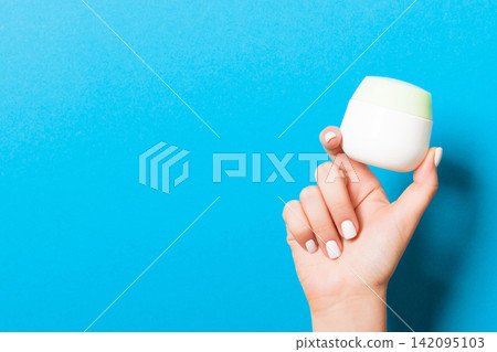 Female hand holding cream bottle of lotion isolated. Girl give jar cosmetic products on blue background Female hand holding cream bottle of lotion isolated. Girl give jar cosmetic products on blue background 142095103