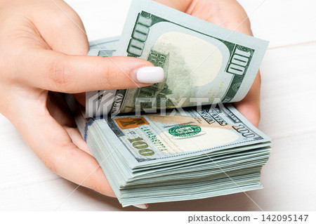 Perspective view of female hands counting money. One hundred dollar banknotes on wooden background. Salary concept. Bribe concept Perspective view of female hands counting money. One hundred dollar banknotes on wooden background. Salary concept. Bribe concept 142095147