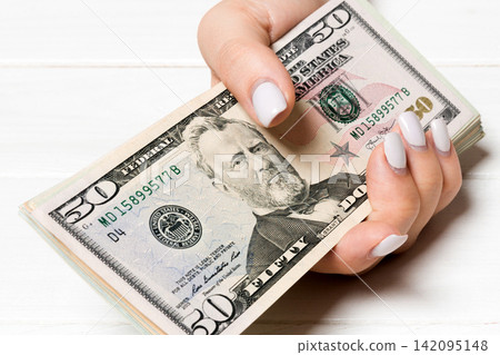 Female hand holding a bundle of money on wooden background. Perspective view of fifty and other dollar banknotes. Salary concept with empty space for your design 142095148