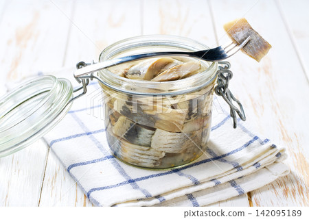 Marinated herring in a jar with herbs on a white table, selective focus. Herring marinated with oil and salt Marinated herring in a jar with herbs on a white table, selective focus. Herring marinated with oil and salt 142095189