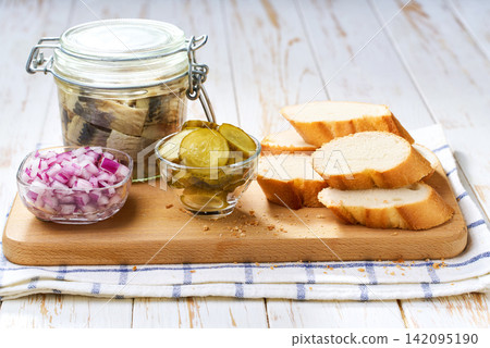 Slices of baguette with pieces marinated herring fillet with with red onions and pickles on table. Slices of baguette with pieces marinated herring fillet with with red onions and pickles on table. 142095190