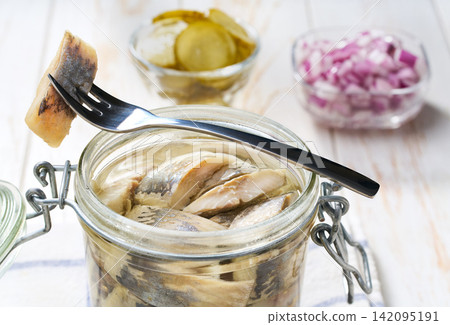 Marinated herring in a jar with herbs on a white table, selective focus. Herring marinated with oil and salt Marinated herring in a jar with herbs on a white table, selective focus. Herring marinated with oil and salt 142095191