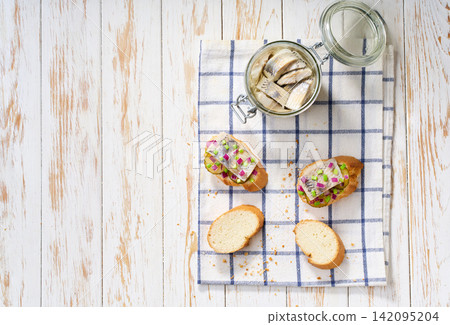 Slices of baguette with pieces marinated herring fillet with with red onions and pickles on table. Top view. Slices of baguette with pieces marinated herring fillet with with red onions and pickles on table. Top view. 142095204