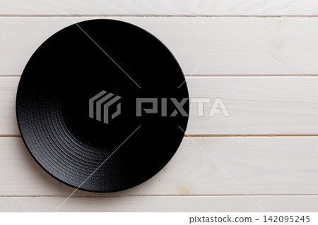 Top view of black plate on wooden background. Empty space for your design Top view of black plate on wooden background. Empty space for your design 142095245