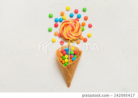 waffle cone full of assorted traditional candies falling out on colored background with copy space. Happy Holidays sale concept waffle cone full of assorted traditional candies falling out on colored background with copy space. Happy Holidays sale concept 142095417