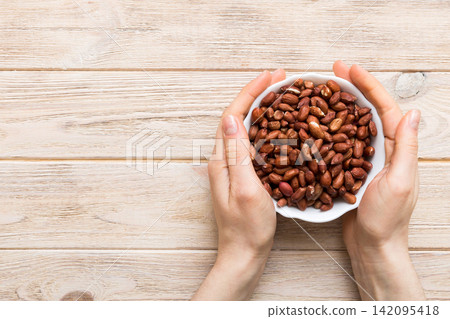 Woman hands holding a wooden bowl with peanuts. Healthy food and snack. Vegetarian snacks of different nuts Woman hands holding a wooden bowl with peanuts. Healthy food and snack. Vegetarian snacks of different nuts 142095418