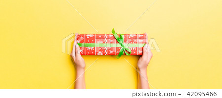 Woman arms holding gift box with colored ribbon on yellow table background, top view and copy space for you design 142095466