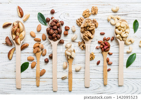 mixed nuts in white wooden spoon. Mix of various nuts on colored background. pistachios, cashews, walnuts, hazelnuts, peanuts and brazil nuts mixed nuts in white wooden spoon. Mix of various nuts on colored background. pistachios, cashews, walnuts, hazelnuts, peanuts and brazil nuts 142095523