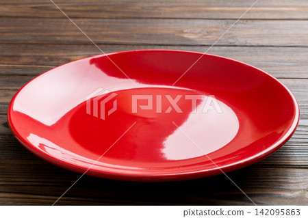 Perspective view of empty red plate on wooden background. Empty space for your design Perspective view of empty red plate on wooden background. Empty space for your design 142095863