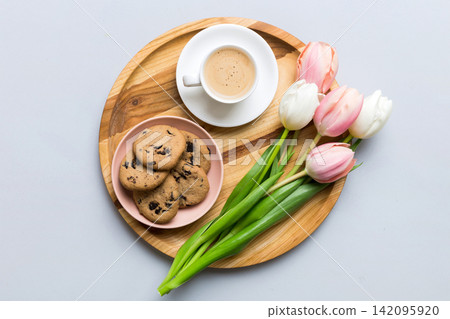 Cup of coffee mug with coffee, cookies and tulips on a colored background. Greeting spring card top view Cup of coffee mug with coffee, cookies and tulips on a colored background. Greeting spring card top view 142095920