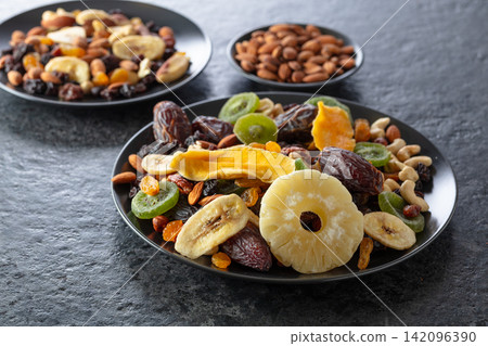 Dried tropical fruits, nuts, and raisins in black plate. Dried tropical fruits, nuts, and raisins in black plate. 142096390