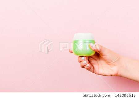 Female hand holding cream bottle of lotion isolated. Girl give jar cosmetic products on pink background 142096615