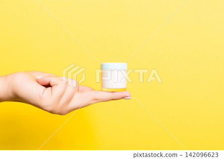 Female hand holding cream bottle of lotion isolated. Girl give jar cosmetic products on yellow background Female hand holding cream bottle of lotion isolated. Girl give jar cosmetic products on yellow background 142096623