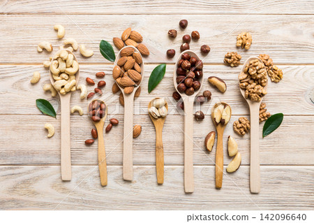 mixed nuts in white wooden spoon. Mix of various nuts on colored background. pistachios, cashews, walnuts, hazelnuts, peanuts and brazil nuts mixed nuts in white wooden spoon. Mix of various nuts on colored background. pistachios, cashews, walnuts, hazelnuts, peanuts and brazil nuts 142096640