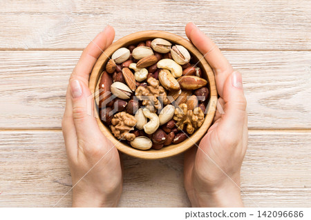 Woman hands holding a wooden bowl with mixed nuts Walnut, pistachios, almonds, hazelnuts and cashews. Healthy food and snack. Vegetarian snacks of different nuts Woman hands holding a wooden bowl with mixed nuts Walnut, pistachios, almonds, hazelnuts and cashews. Healthy food and snack. Vegetarian snacks of different nuts 142096686