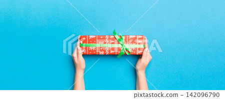 Woman arms holding gift box with colored ribbon on blue table background, top view and copy space for you design Woman arms holding gift box with colored ribbon on blue table background, top view and copy space for you design 142096790