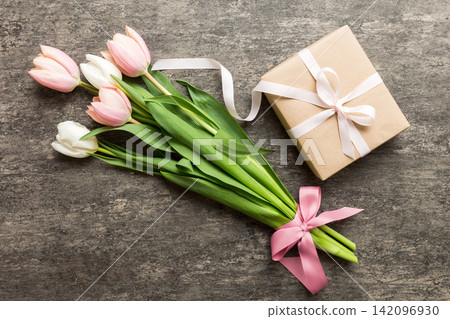 Pink tulips flowers and gift or present box on colored table background. Mothers Day, Birthday, Womens Day, celebration concept. Space for text top view Pink tulips flowers and gift or present box on colored table background. Mothers Day, Birthday, Womens Day, celebration concept. Space for text top view 142096930