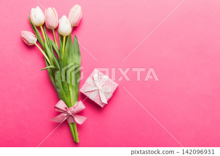 Pink tulips flowers and gift or present box on colored table background. Mothers Day, Birthday, Womens Day, celebration concept. Space for text top view Pink tulips flowers and gift or present box on colored table background. Mothers Day, Birthday, Womens Day, celebration concept. Space for text top view 142096931