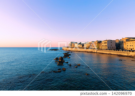 A picturesque coastal city awakens with the soft hues of dawn painting the sky above the tranquil sea and historic buildings A picturesque coastal city awakens with the soft hues of dawn painting the sky above the tranquil sea and historic buildings 142096970