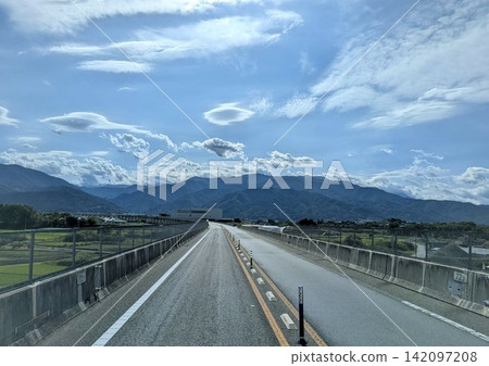 A road stretching towards a vast blue sky and majestic mountain range. A road stretching towards a vast blue sky and majestic mountain range. 142097208