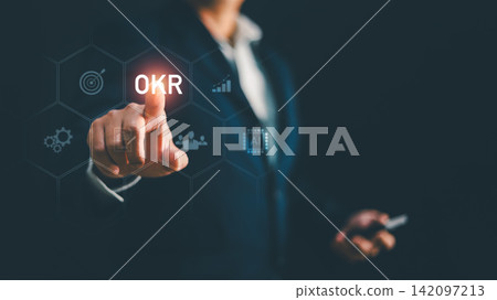 Businessman touching glowing OKR text on futuristic screen with target graph icon. Concept for business goal management, objective key result, strategic planning, performance tracking, corporate Businessman touching glowing OKR text on futuristic screen with target graph icon. Concept for business goal management, objective key result, strategic planning, performance tracking, corporate 142097213