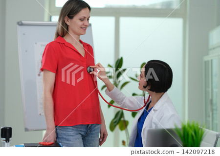 Woman cardiologist listens to patient heartbeat with stethoscope 142097218