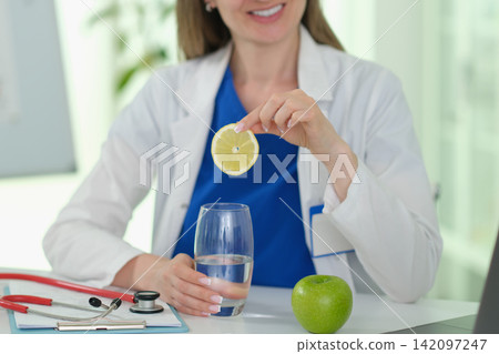 Happy lady doctor puts lemon slice into water glass in hospital 142097247