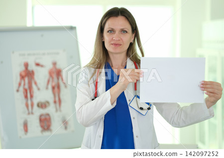 Woman doctor holds blank paper sheet as stands in medical office Woman doctor holds blank paper sheet as stands in medical office 142097252