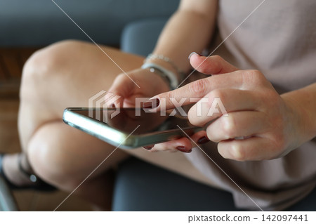 Engaging with technology while seated in a cozy living room, sending messages on a smartphone Engaging with technology while seated in a cozy living room, sending messages on a smartphone 142097441