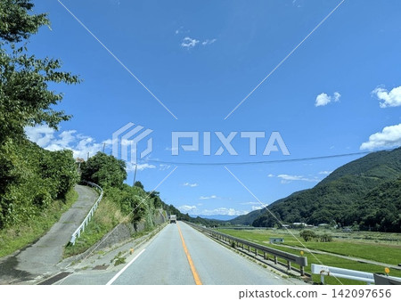 A summer road stretches straight across the fields and mountains under a blue sky. A summer road stretches straight across the fields and mountains under a blue sky. 142097656