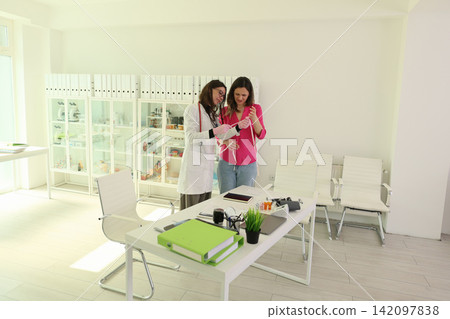 Female doctor measures woman waist with tape inside bright modern clinic office, health consultation scene with medical cabinet, desk, chairs, and daylight interior, personal wellness assessment Female doctor measures woman waist with tape inside bright modern clinic office, health consultation scene with medical cabinet, desk, chairs, and daylight interior, personal wellness assessment 142097838