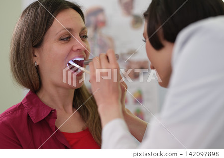 Woman doctor checks patient throat during clinic examination Woman doctor checks patient throat during clinic examination 142097898