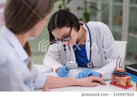 Woman doctor examines lady patient skin with magnifying glass Woman doctor examines lady patient skin with magnifying glass 142097929