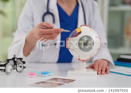 Woman doctor explains eyeball model during vision examination Woman doctor explains eyeball model during vision examination 142097930