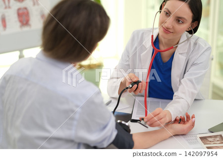 Woman doctor checks patient blood pressure during clinic visit Woman doctor checks patient blood pressure during clinic visit 142097954
